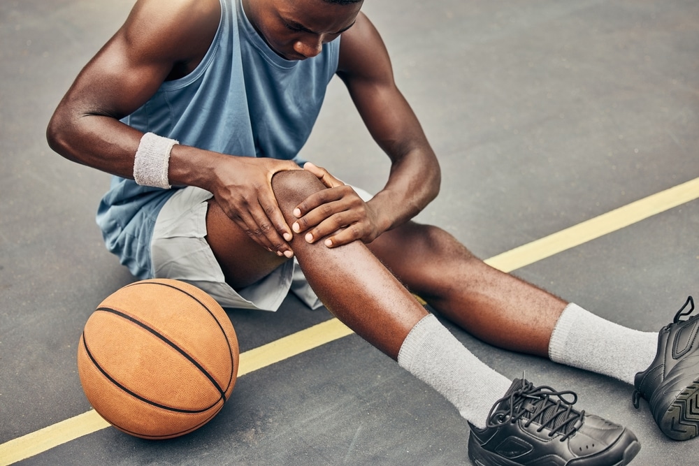 Man sitting on ground holding knee after getting injured playing basketball.